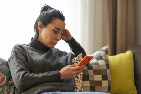 Sad woman looking at mobile phone screen at home